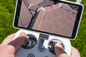 roof inspection. Hands holding a drone remote with screen to see the top of a roof