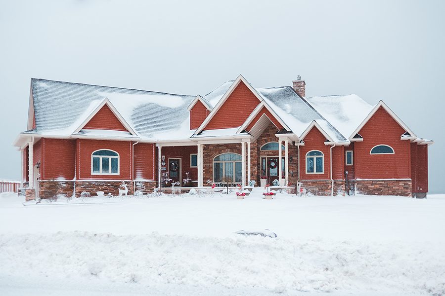 Roofing in winter. Winter roofing showing a large red house decorated for the holidays with a dusting of snow.