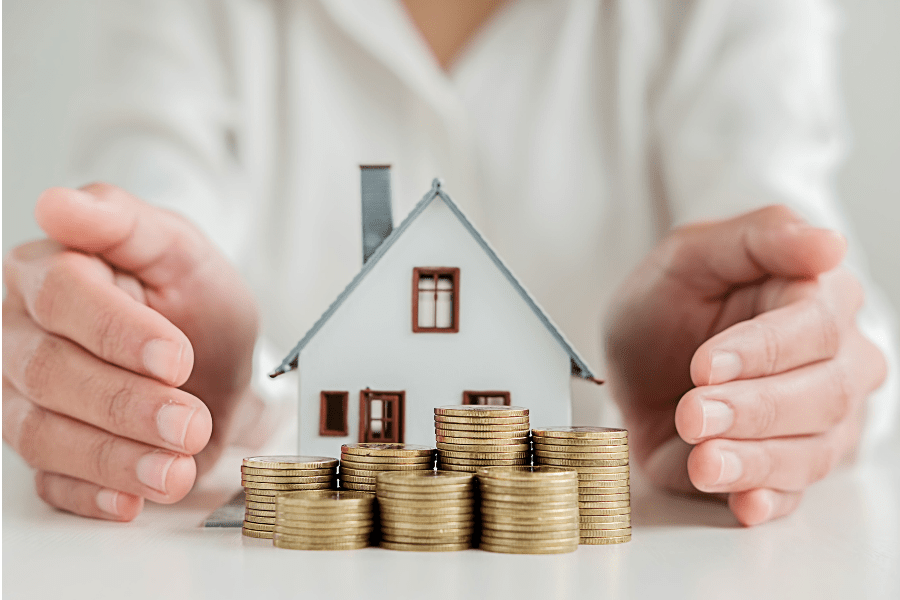 roof maintenance tips: showing a tiny dollhouse in between two hands with piles of gold coins out front.