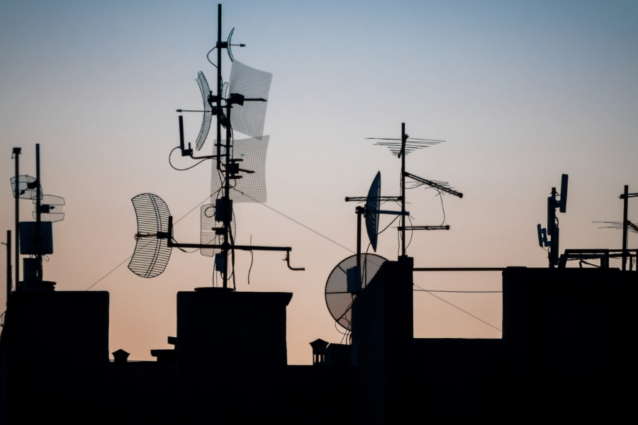 attaching to roofing: showing a bunch of antennas attached to roofs backlit by the sunset.
