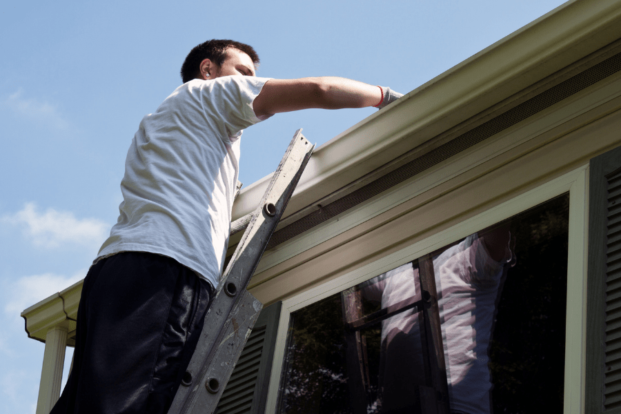 Home Gutters, showing a man standing on a ladder working on his gutters.